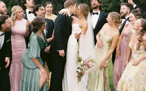 A wedding party celebrates as the bride and groom kiss. The groomsmen attire is classic black tuxedos.