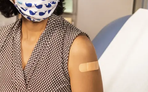 Osoba w maseczce z wielorybami ma plaster na ramieniu po szczepieniu. Dbanie o zdrowie, w tym szczepionka HPV, to ważny krok.