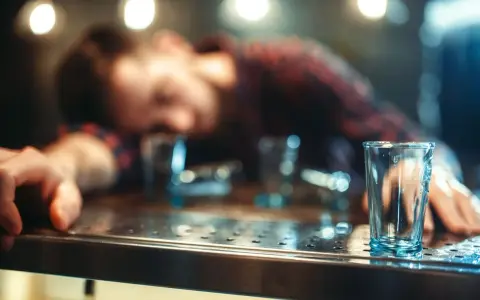 Ostatnia nadzieja na wytrzeźwienie: pusta szklanka na barze obok śpiącego mężczyzny.