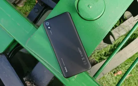 Czarny telefon Xiaomi Redmi 7 leży na zielonej, metalowej ławce.