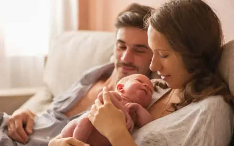 Mama tuli noworodka, tata patrzy z miłością. To piękny obraz opieki na żone po porodzie, pełen czułości i wsparcia.