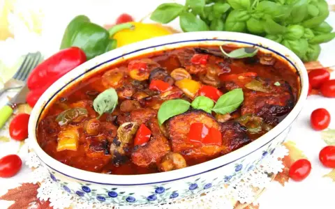 Schab po cygańsku z pieczarkami i papryką w sosie pomidorowym, udekorowany bazylią. Danie wygląda apetycznie.