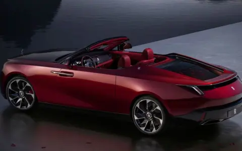 Czerwony kabriolet Rolls-Royce, najdroższe auto na świecie, lśni przy wodzie.