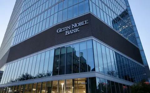 Nowoczesny budynek banku z napisem "GETIN NOBLE BANK". W szklanej fasadzie odbijają się inne budynki i drzewa.