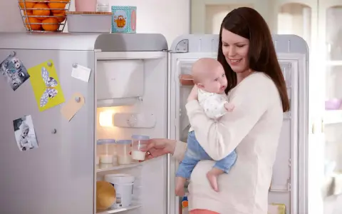 Mama z dzieckiem przy lodówce, gdzie przechowywanie mleka matki jest łatwe dzięki specjalnym pojemnikom.