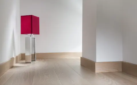 Enkel golvlistsinspiration i ljust trä som ramar in ett modernt rum med en röd bordslampa.