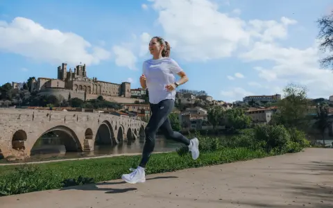 Kobieta biegnie wzdłuż rzeki, mijając zabytkowy most i miasto. Zastanawia się, ile się biegnie 5 km.