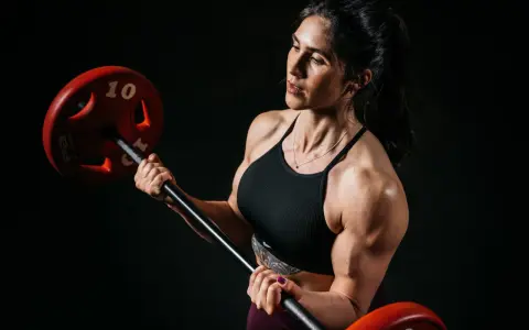 Eine starke Bodybuilderin Frau hebt eine Hantel. Ihre Muskeln sind deutlich sichtbar.