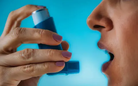 Person nutzt Asthmaspray vor oder nach dem Sport. Die Hand hält das blaue Gerät, der Mund ist geöffnet.