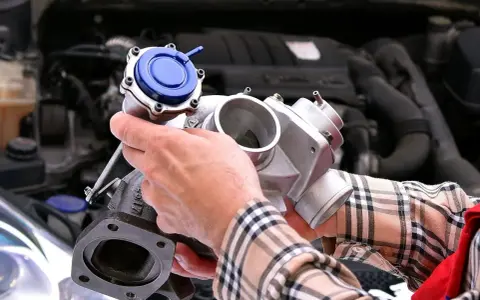 Mechanik trzyma turbosprężarkę, pokazując, gdzie znajduje się czujnik ciśnienia doładowania.