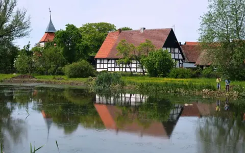 Swołowo kraina w kratę. Domki z muru pruskiego odbijają się w stawie, a w oddali widać kościół.