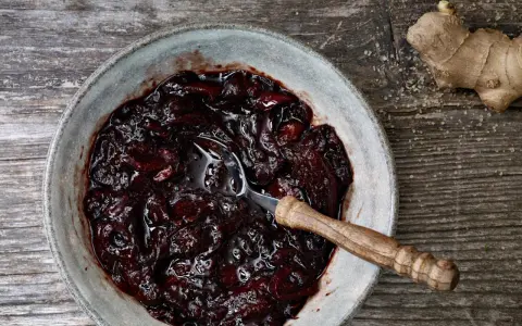 Dunkles, glänzendes Zwetschgen-Chutney in einer Schale, daneben ein Stück Ingwer und Zucker.