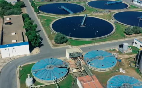 Vista aérea de una planta de depuración de aguas con grandes tanques circulares y estructuras industriales.