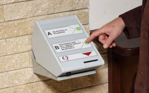 Dłoń naciska przycisk na automacie do wydawania dokumentów rejestracyjnych.