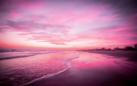 Spiaggia di Riccione immersa nel rosa della Notte Rosa, con il mare calmo e il cielo infuocato.