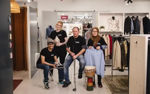 Fyra personer poserar i en butik med kläder och föremål. En kvinna håller en vas, en man en golfklubba, och en annan kvinna en ljusblå hoodie. De representerar hållbart second hand.