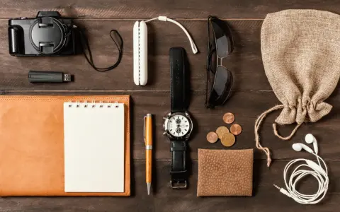 Zestaw EDC: aparat, pendrive, notes, długopis, zegarek, okulary, monety, portfel, słuchawki i woreczek.