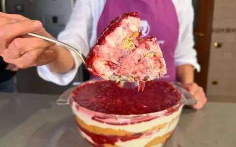 Un cucchiaio solleva una porzione generosa di un goloso tiramisù alle fragole, stratificato con crema e biscotti, pronto per essere gustato.