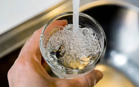 En hand håller ett glas som fylls med vatten från en kran. Bubblor bildas i vattnet, vilket kan tyda på klor i dricksvatten.
