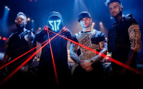 Czterech mężczyzn w futurystycznych strojach, z maską LED i czerwonymi laserami na scenie.