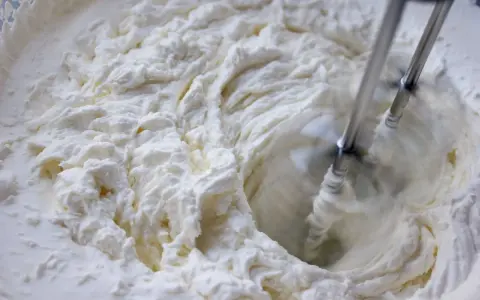 Batidora eléctrica batiendo crema blanca y espesa en un bol.