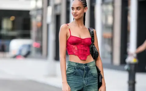 Frau mit geflochtenen conros Haare trägt ein rotes Korsett-Top und Jeans.