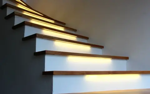 Nowoczesne lampy na klatkę schodową subtelnie oświetlają drewniane stopnie, tworząc ciepłą i bezpieczną atmosferę.