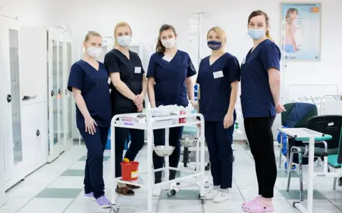 Pięć studentek pielęgniarstwa w granatowych uniformach i maseczkach stoi przy wózku medycznym. To ich przyszła praca dla studenta pielęgniarstwa.