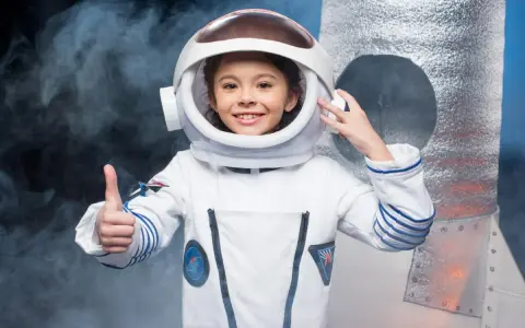 Niña sonriente con un disfraz de universo casero de astronauta, pulgar arriba, lista para explorar.