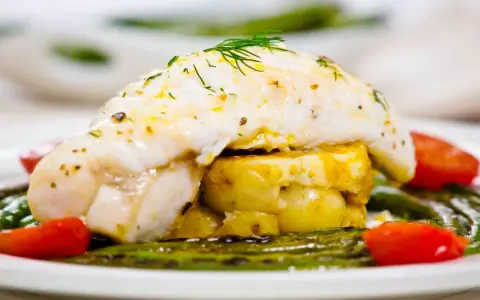Ein zarter Seeteufel ruht auf Kartoffeln, umgeben von grünem Spargel und Tomaten. Ein köstliches Gericht, das an das Meer erinnert.