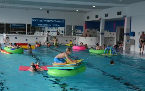 Kinder und Erwachsene planschen im Nichtschwimmerbereich des Schwimmbads Brakel. Viele nutzen bunte Schwimmtiere und Matten.