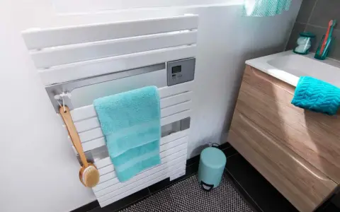 Un sèche-serviettes blanc moderne, avec une serviette turquoise et une brosse de bain en bois. La hauteur du sèche-serviette est idéale pour un accès facile.