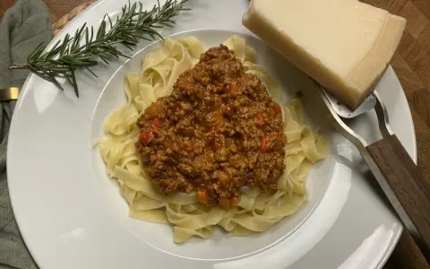 Ein Teller Tagliatelle mit herzhafter Bolognese, garniert mit Rosmarin und Parmesan.