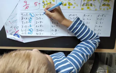 Dziecko rozwiązuje zadania matematyczne. Na kartce widać różne działania, a obok nich cyfry, które mogą stanowić **skalę ocen** lub odpowiedzi.