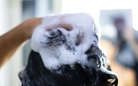 Mano che massaggia shampoo schiumoso sui capelli scuri, puliti o sporchi, per un momento di relax.