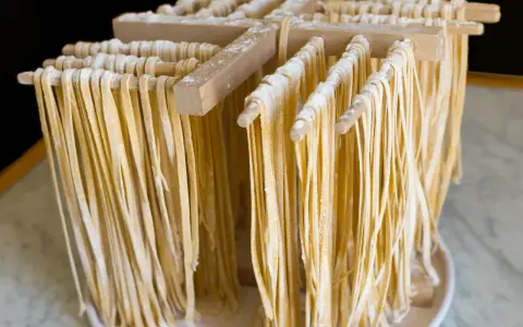 Świeżo przygotowany, domowy makaron tagliatelle suszy się na drewnianym stojaku.