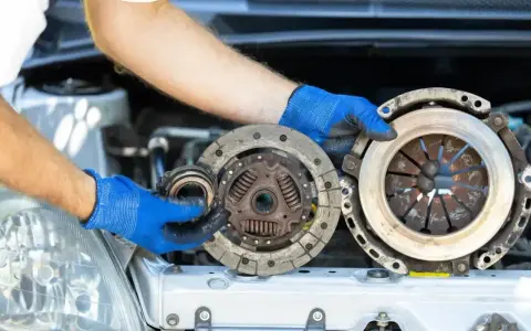 Mechanik w niebieskich rękawiczkach pokazuje zużyte części sprzęgła, które mogą być przyczyną ślizgającego się sprzęgła objawy.