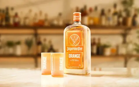 Butelka Jägermeister Orange i dwa kieliszki z napisem "ORANGE" na blacie. Idealny zestaw na letnie wieczory.