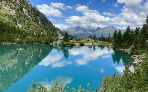Lago alpino cristallino, perfetto per passeggiate in montagna Lombardia. Riflessi di cielo e montagne.