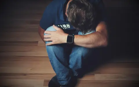 Mężczyzna siedzi skulony na podłodze, opierając głowę na kolanach.