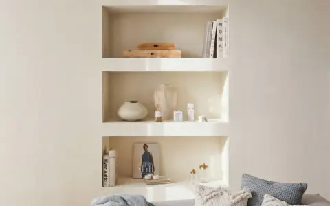 Una nicchia nel muro del salotto, con libri, vasi e diffusore, crea un angolo accogliente e ordinato.