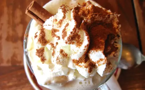 Un déliceux café liégeois recette : crème fouettée, cacao et bâton de cannelle dans un verre.