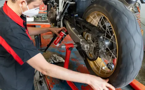Meccanico lubrifica la catena di una moto. La pulizia catena moto ogni quanti km è fondamentale per la sua durata.