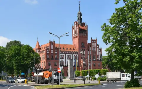 Imponujący ratusz w Słupsku, jedna z głównych atrakcji miasta, góruje nad placem. W tle zielone drzewa i błękitne niebo.