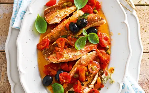 Deliziosa gallinella di mare in umido con pomodorini, olive nere e capperi, guarnita con basilico fresco.