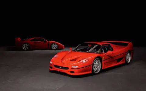 Zwei rote Ferraris, ein F50 und ein F40, stehen nebeneinander auf dunklem Grund.