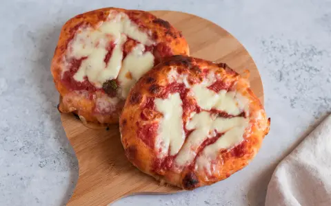 Due pizzette fatte in casa, con pomodoro e mozzarella filante, su un tagliere di legno.