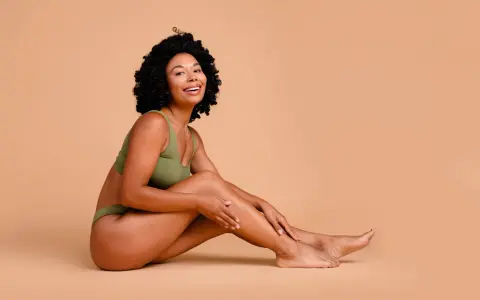 Femme souriante en sous-vêtements verts, caressant sa jambe. Elle partage ses secrets pour comment avoir des pieds doux.