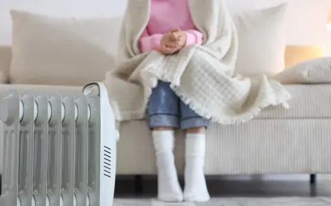 Radiador eléctrico junto a un sofá donde una persona se abriga. Una solución eficaz para los sistemas de calefacción del hogar.