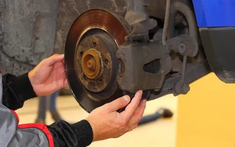 Mechanik sprawdza klocki hamulcowe, dotykając zacisku i tarczy hamulcowej.